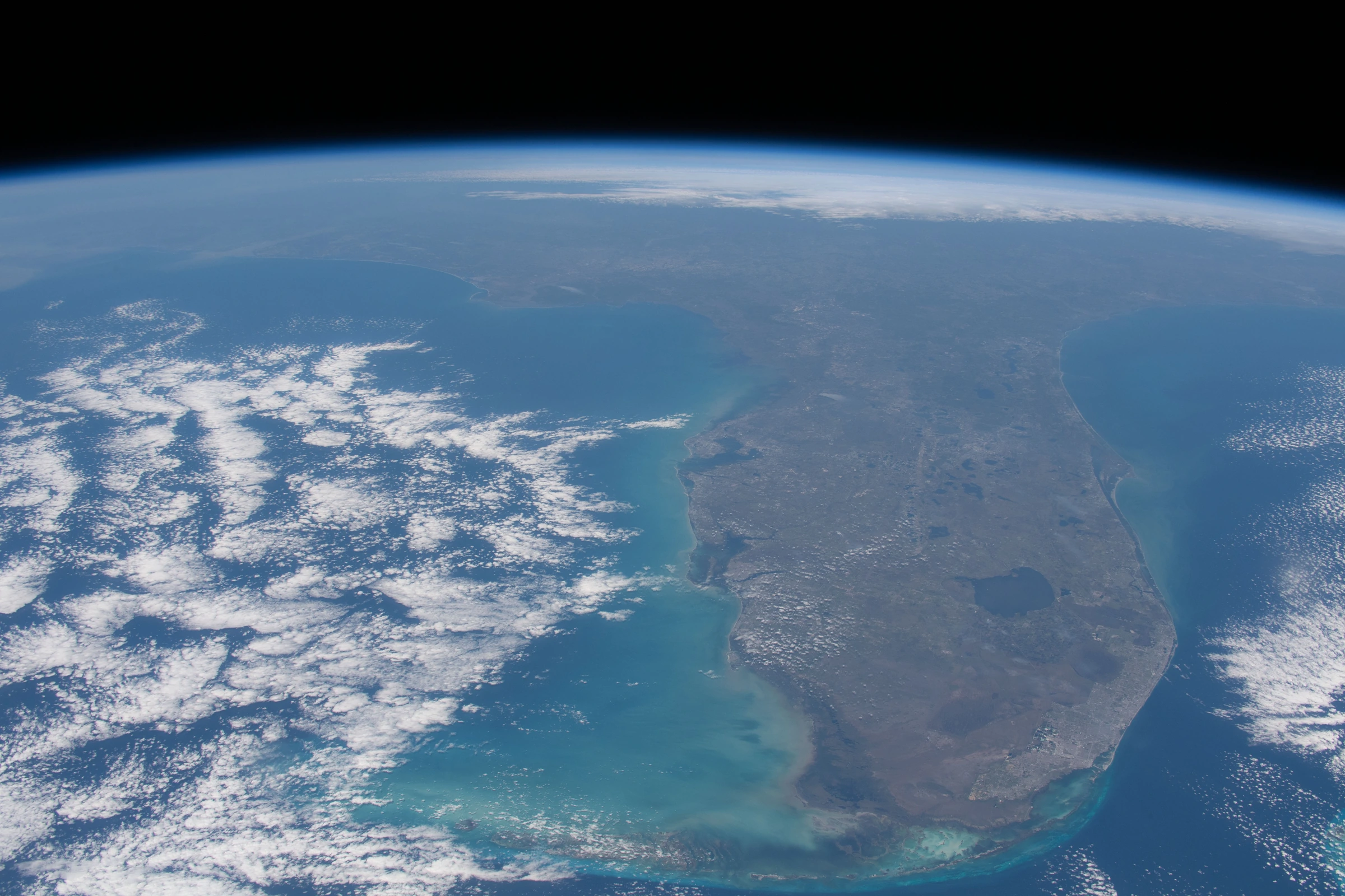 Florida's peninsula and turquoise coast seen from orbit, beneath Earth's curved horizon